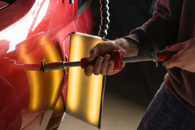 Man performing paintless dent repair in San Antonio on a red Sedan