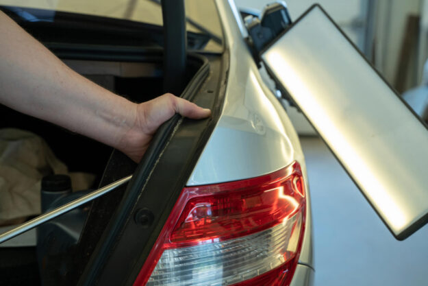 A person using a tool to repair a dent on a silver car's rear panel.