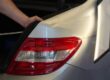 Paintless dent repair technician works on removing a dent from the bumper of a silver sedan.