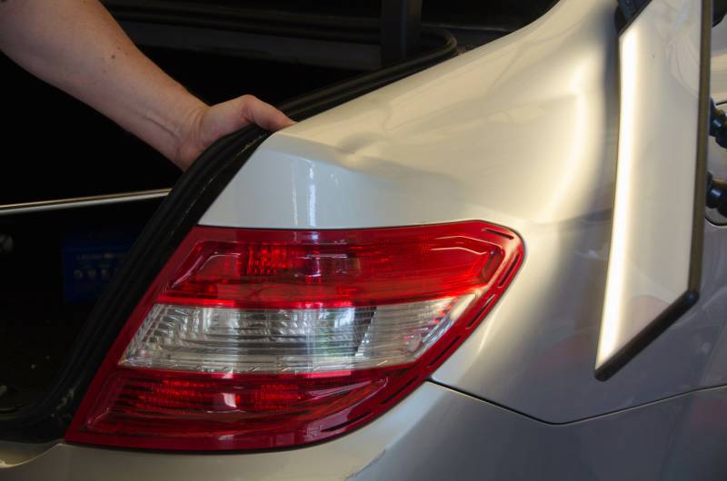 Paintless dent repair technician works on removing a dent from the bumper of a silver sedan.