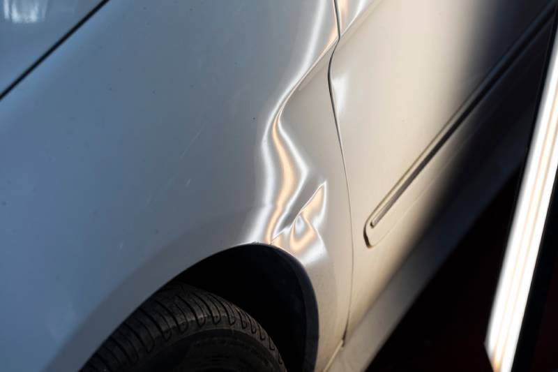 Paintless dent repair concept. Close up on dent behind the back passenger side door of a white sedan.