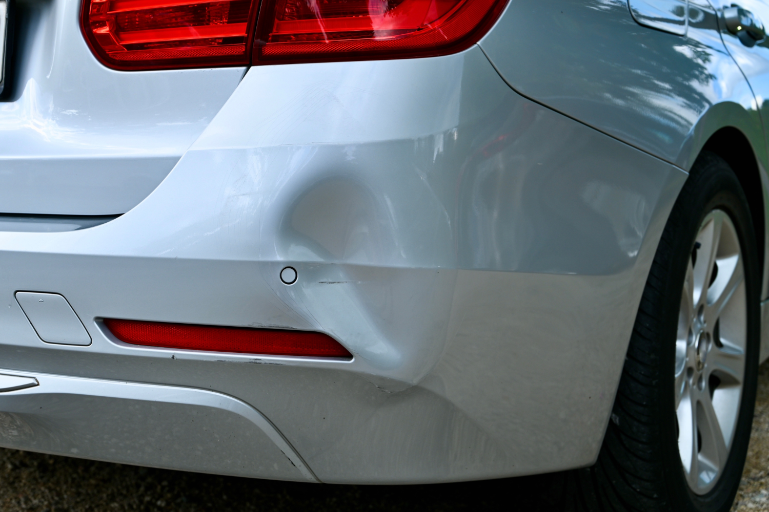 Silver sedan with dent in the back bumper.