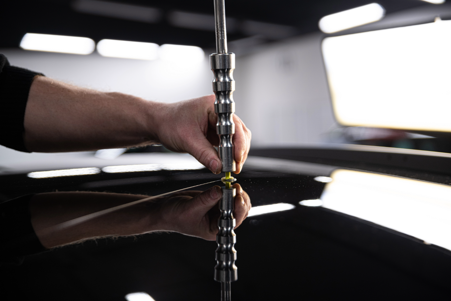 Employee of the car detailing studio removes minor dents from the roof of the car. Closeup on his hands and the tool.